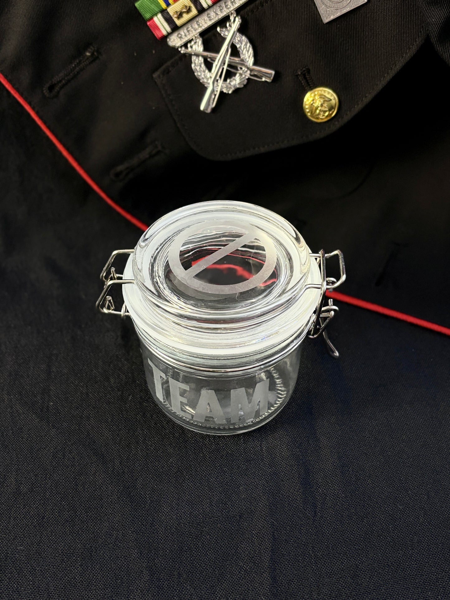 Clear glass jar with TEAM etched into it, with a smell proof lid on a dark surface