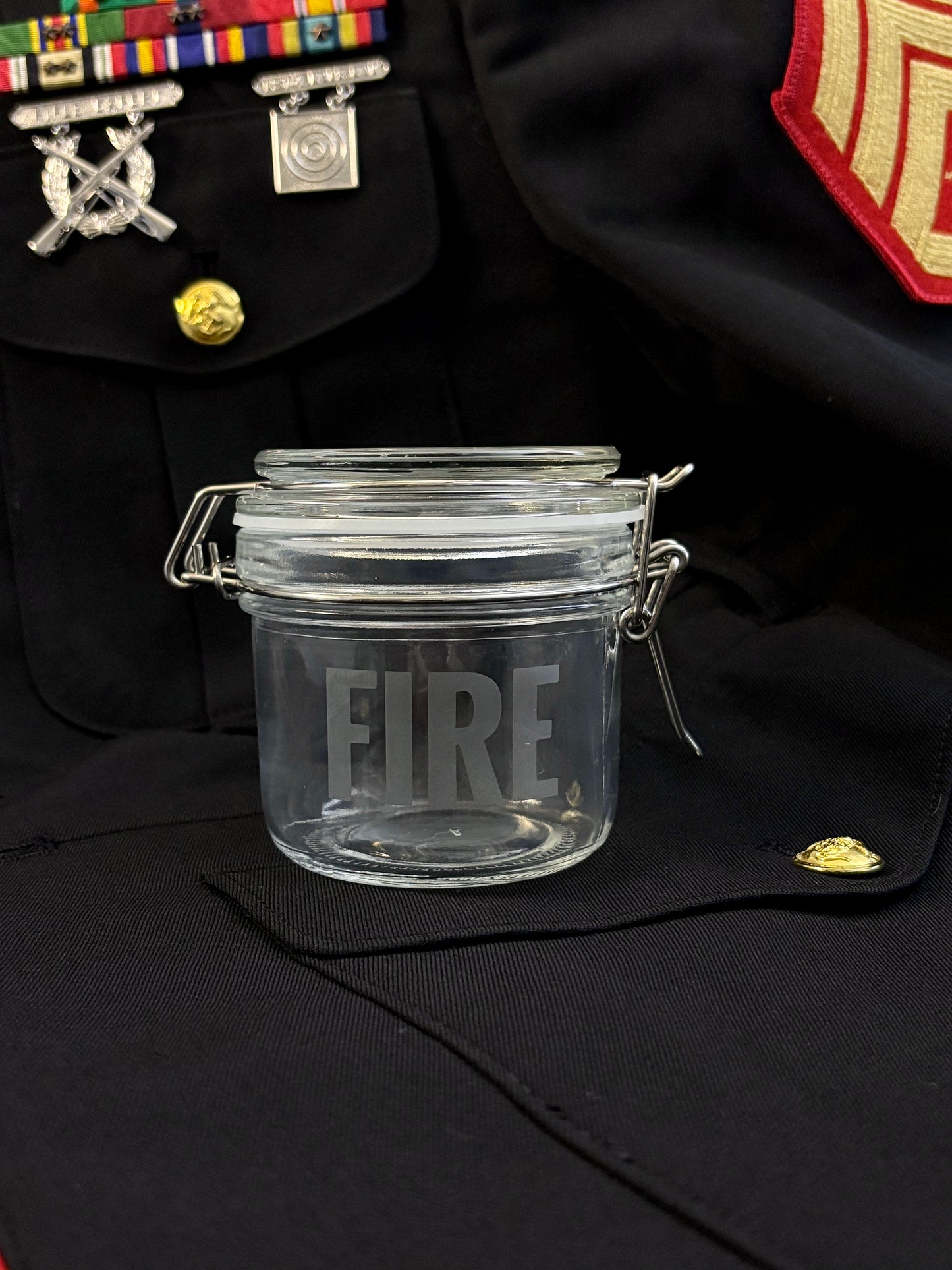 Clear glass jar with 'FIRE' engraving on a black uniform background