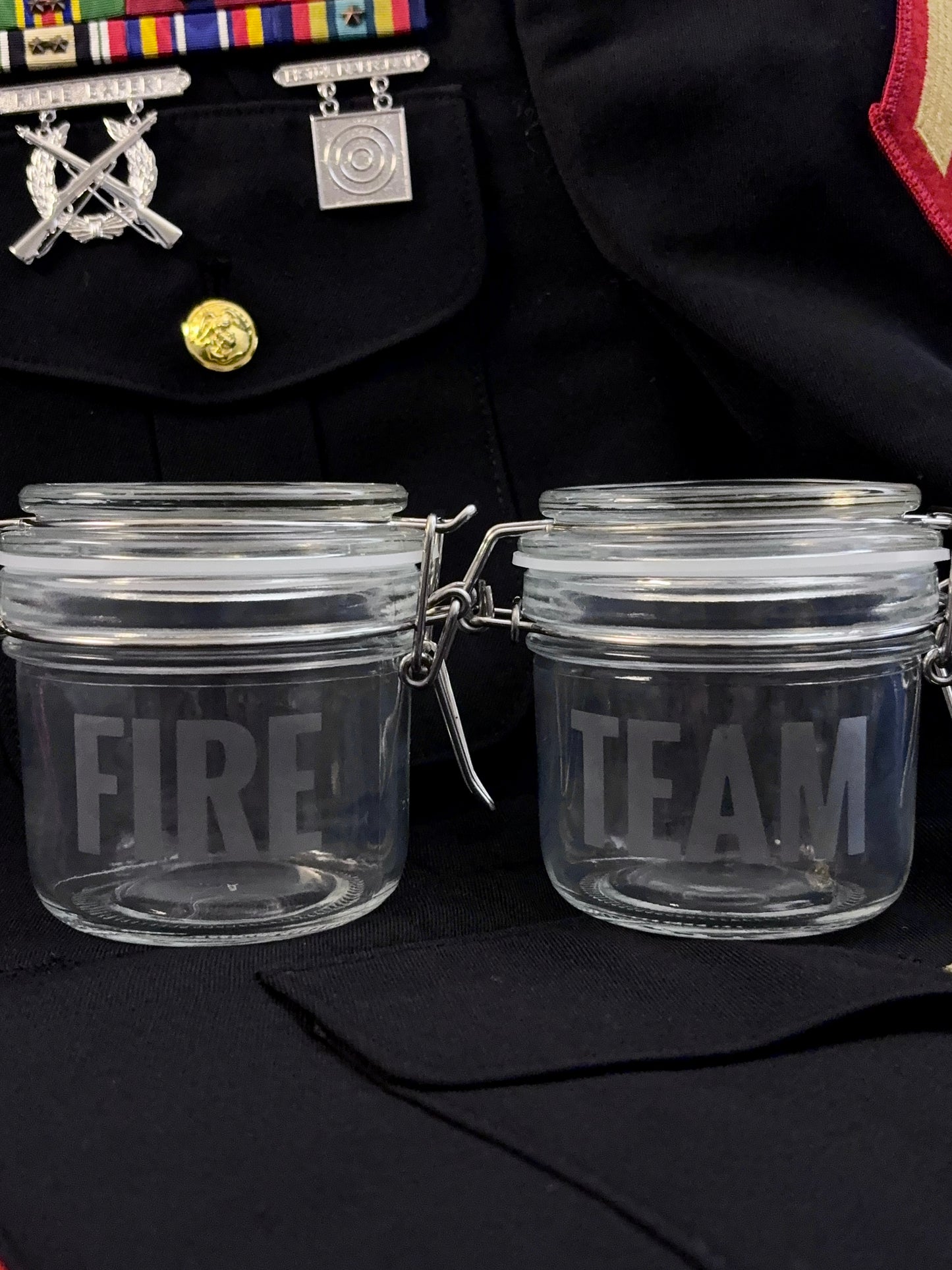 Two clear glass jars labeled 'FIRE' and 'TEAM' on a dark uniform background.